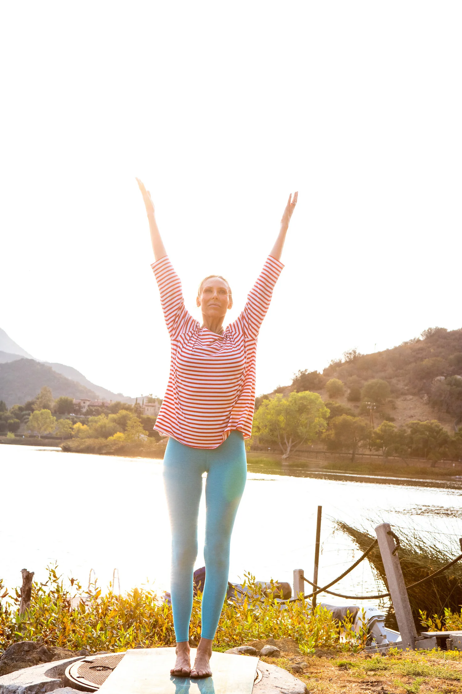 Carolina Goldberg standing with arms raised beside a lake at sunrise