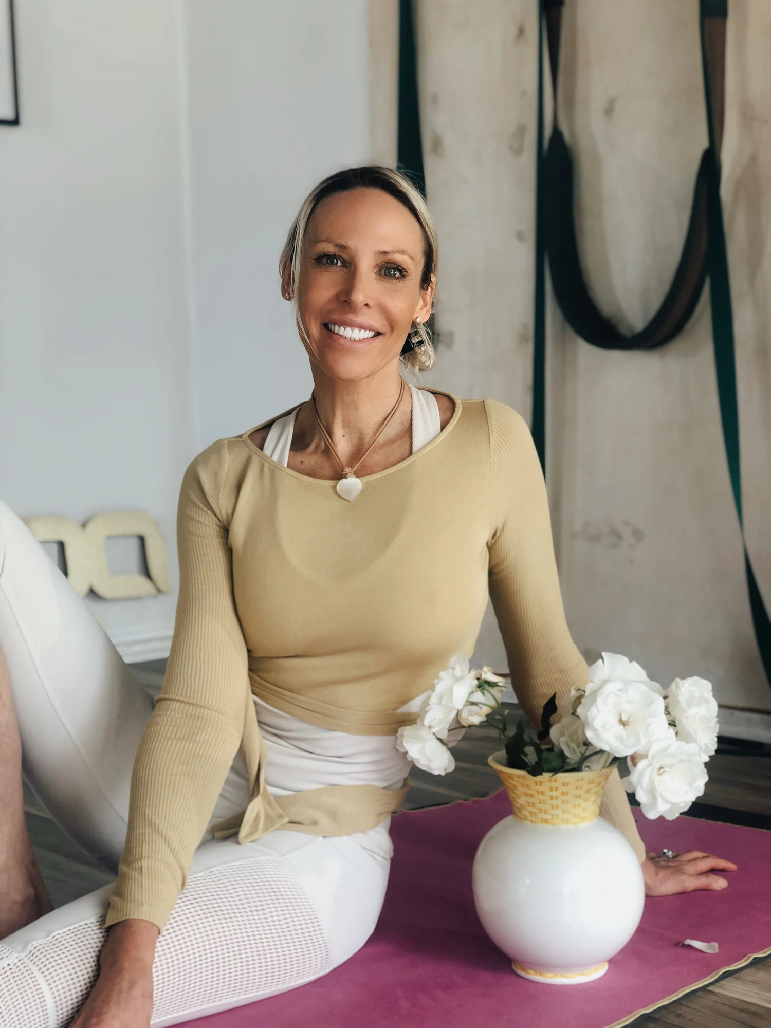 Carolina Goldberg seated on a mat in her studio wearing a selenite pendant